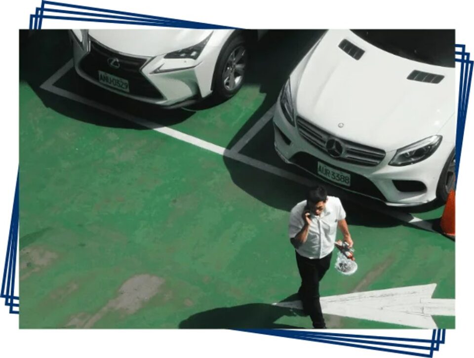 Cars parked in marked airport parking bays with a traveller walking through the lot