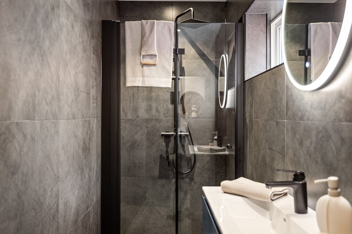 Grey-tiled bathroom with black shower fixtures and a circular mirror