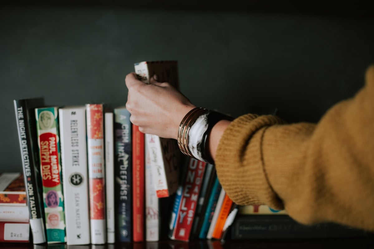 Hand selecting a book from a bookshelf
