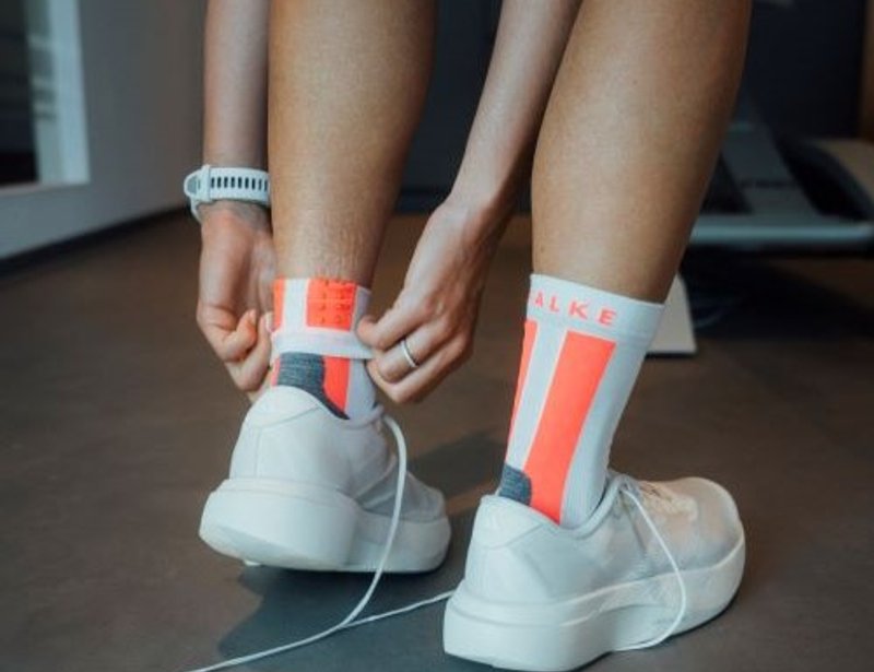 Person zieht eine helle FALKE Sportsocke am Bein hoch