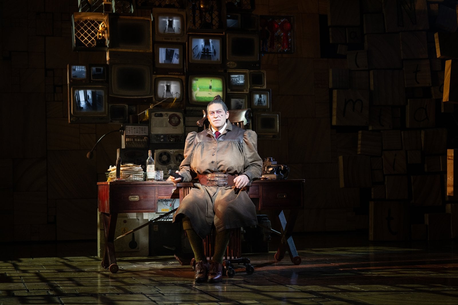Trunchbull seated at a desk in a Matilda The Musical stage scene