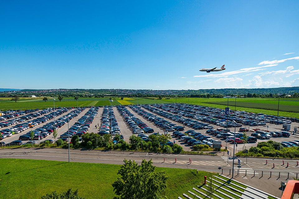 Airport parking area beside a runway with an aircraft overhead