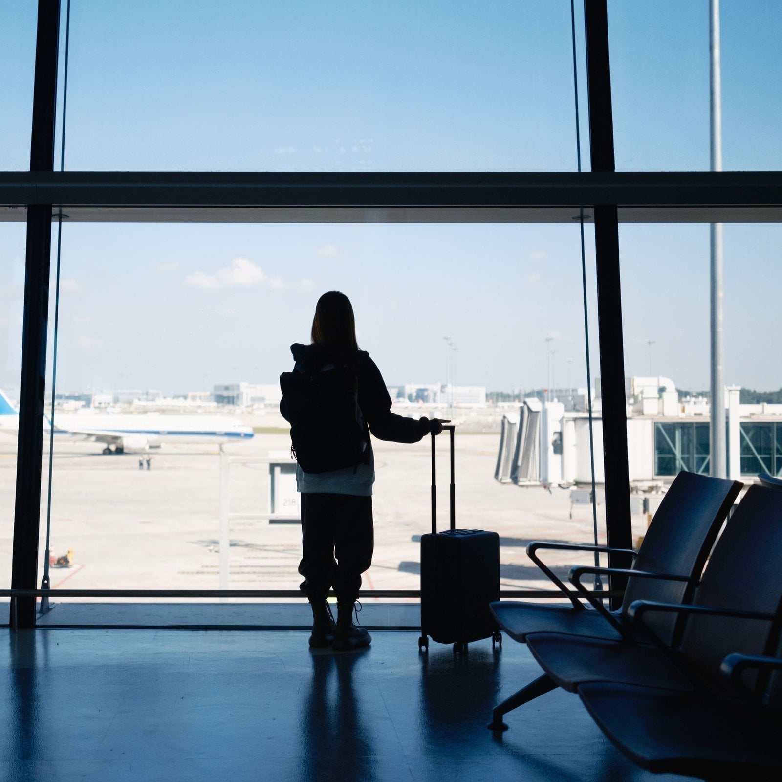 Passenger with suitcase waiting beside airport terminal windows