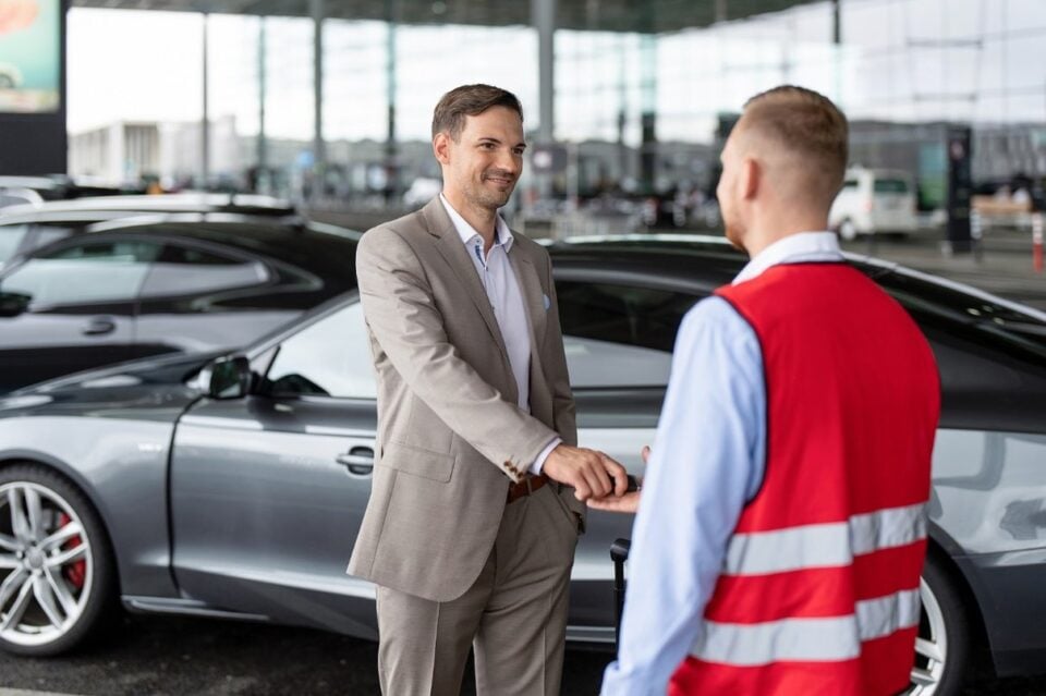 Valet attendant exchanging keys with a traveller beside a car under a terminal canopy