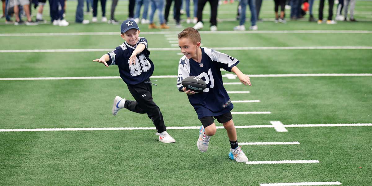 Young fans running with a football on the AT&T Stadium field