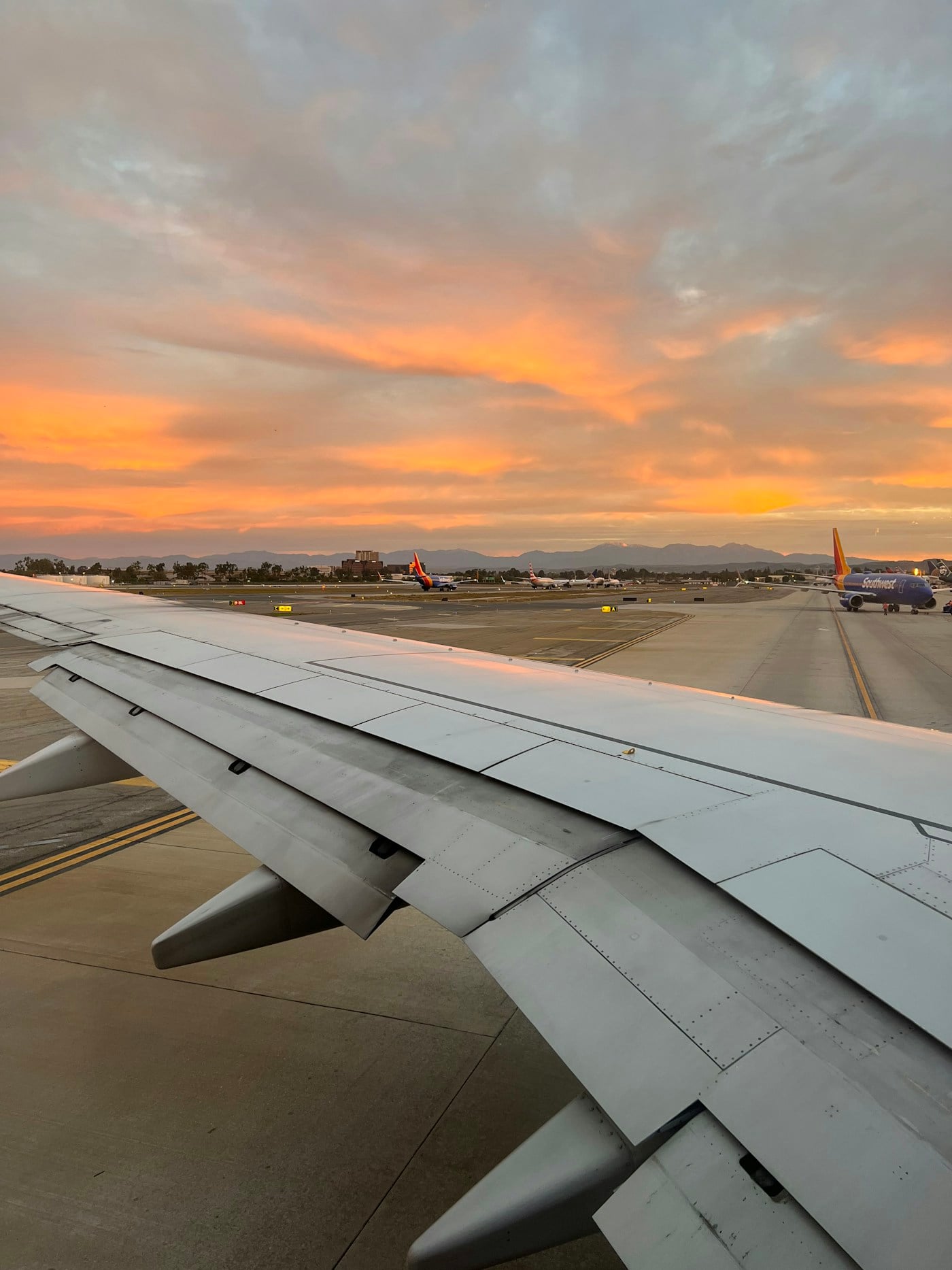 Airplane wing above an airport runway at sunset