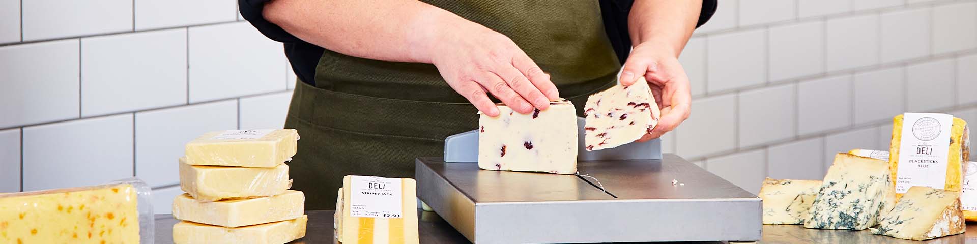 A Morrisons deli worker cutting cheese at the counter