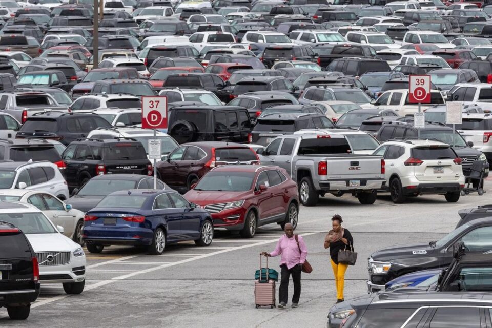 Travellers with luggage walking between rows of cars in a busy airport car park