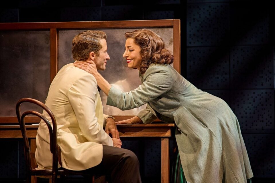 Two performers share a quiet moment at a table on the Sinatra the Musical set
